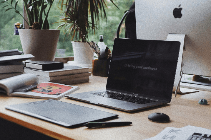 Un bureau moderne avec un ordinateur portable affichant le message 'Driving your business', entouré de livres, un carnet, et des plantes.